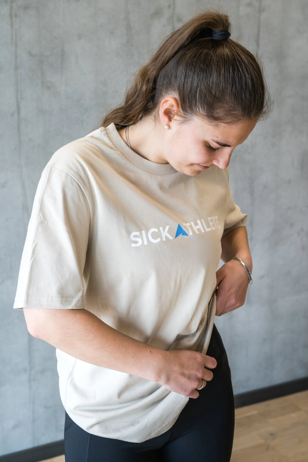 Frau richtet ihre Leggins und zieht dabei ihr SICKATHLETE ESSENTIAL T-Shirt hoch