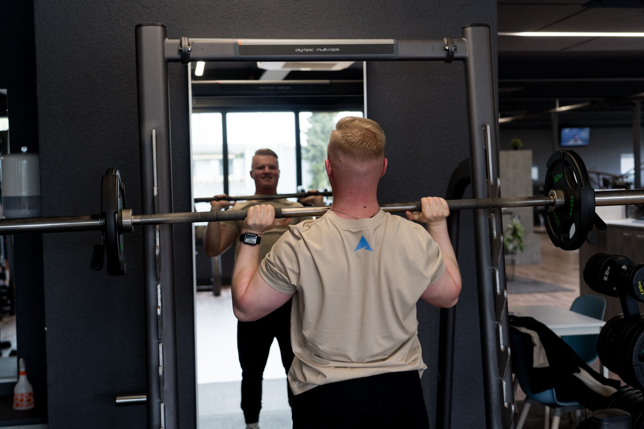 Athlet trainiert im Gym vor dem Spiegel seine Schultern und trägt dabei ein T-Shirt von SICKATHLETE