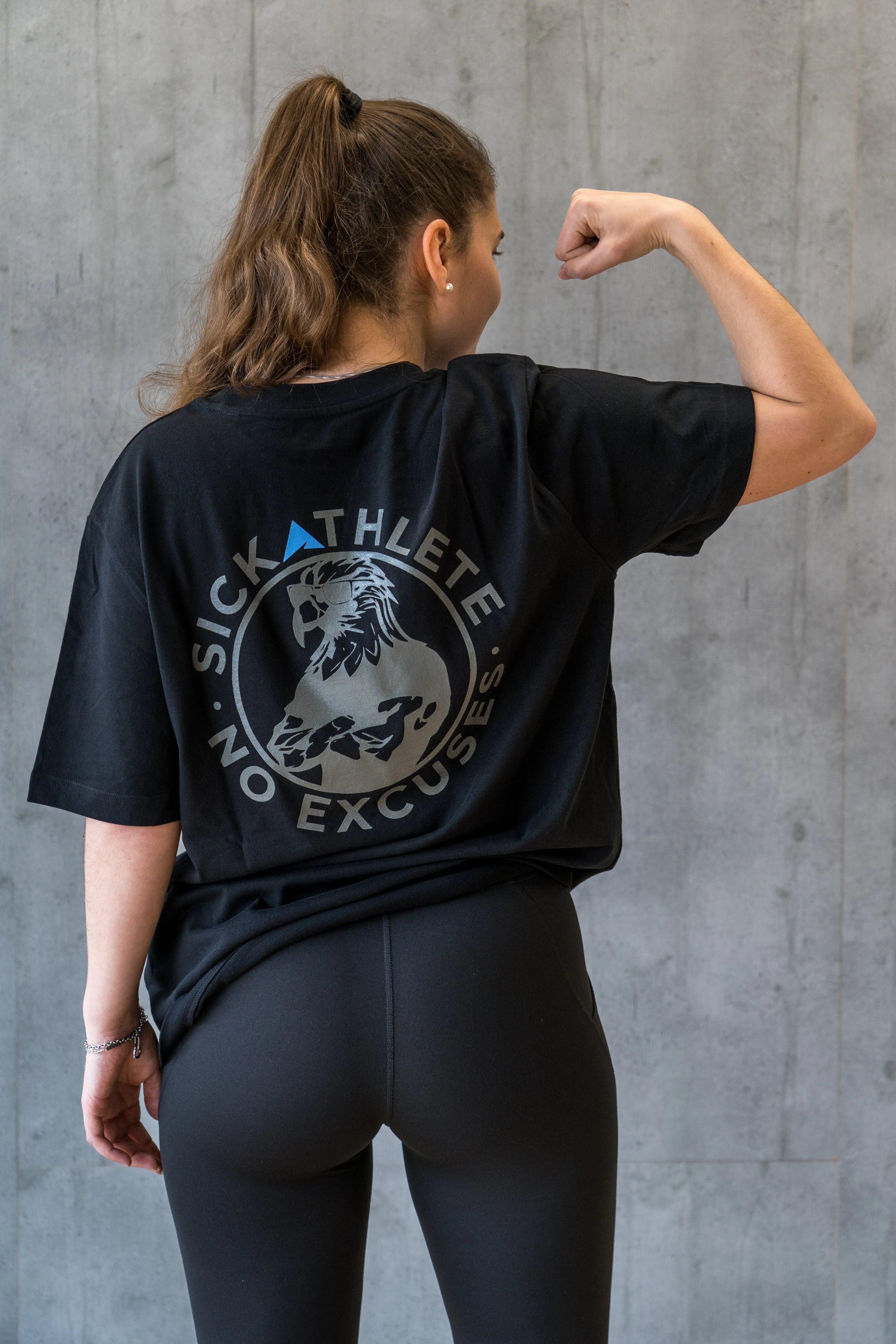 Athletin flext ihren Bizeps im PURPOSE T-Shirt von SICK ATHLETE
