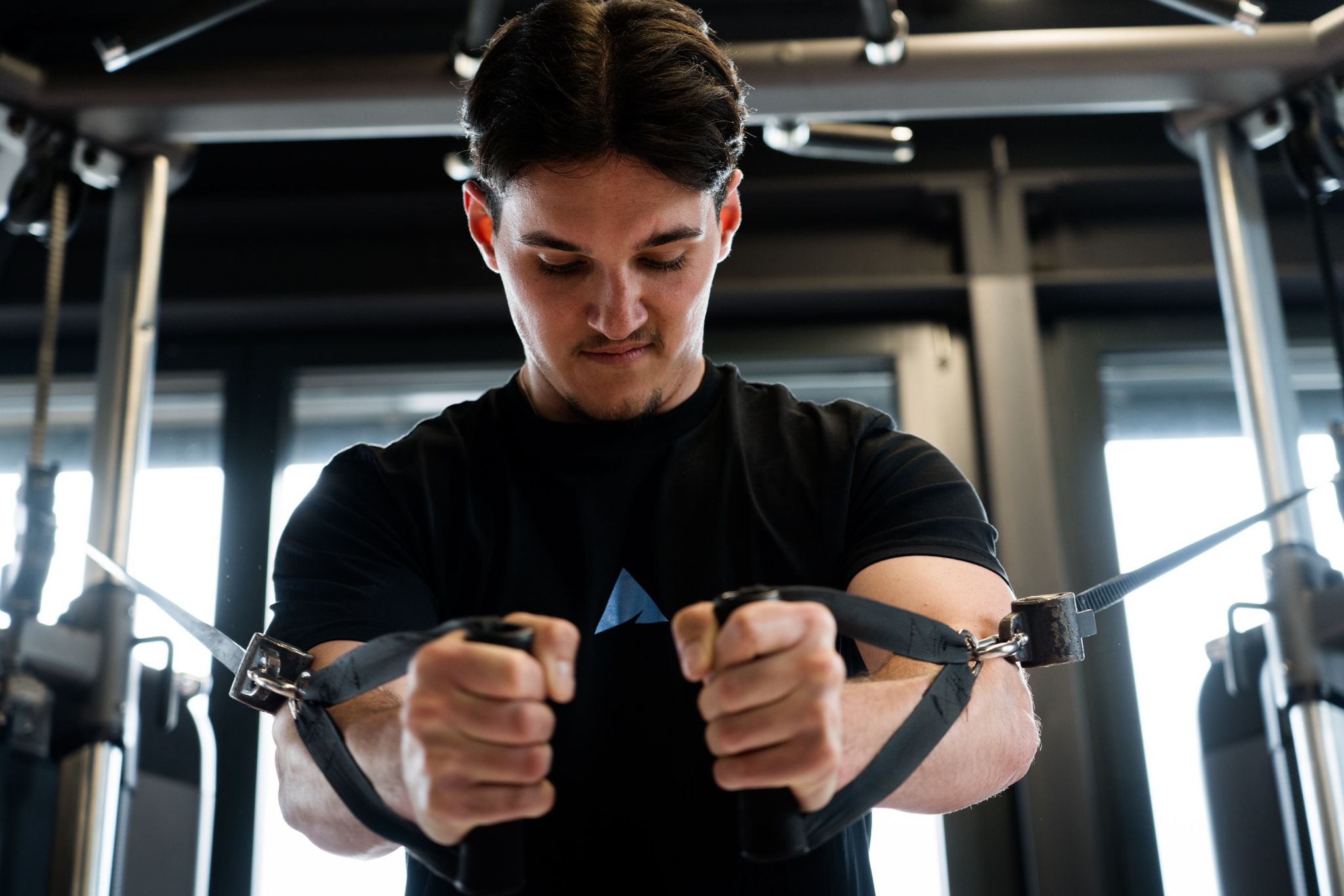 Athlet der im Gym mit seinem Sickathlete T-Shirt am Seilzug seine Brust trainiert